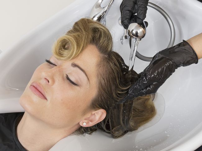 Image symbole: Une cliente se fait laver les cheveux par une personne portant des gants.
