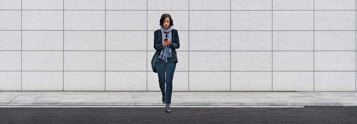Une femme regarde son téléphone portable en traversant une rue.