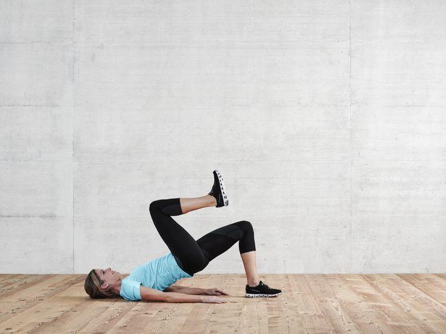 une femme en tenue de sport fait un demi-pont. Elle lève le genou droit, vers la poitrine.