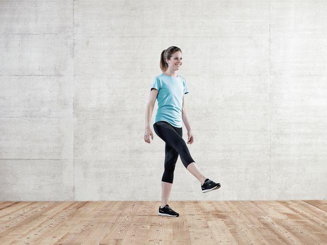 Eine Frau in Sportkleidung macht eine Übung: Sie steht auf dem linken Bein und hält das rechte Bein gestreckt nach vorne-oben.