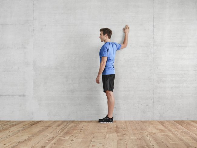 A una parete, un uomo esegue un esercizio di allungamento dei muscoli pettorali.Ha il gomito piegato all’altezza della spalla.