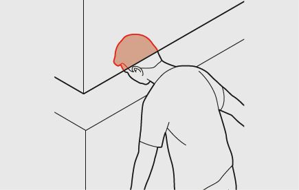 Un membro del personale tiene la testa in un'apertura tra due piani orizzontali. Lo spazio minimo tra questi due piani è in questo caso di 300 mm. La testa è colorata di rosso.