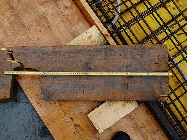 Aufnahme des gebrochenen Gerüstbretts mit einem darüber gelegten Metermass. Das Brett weist eine ausgesägte Stelle auf, wo sich auch die Bruchstelle befindet.