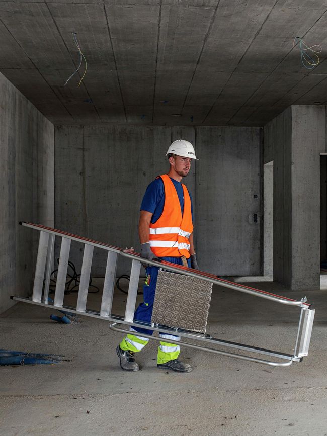 Un ouvrier du bâtiment porte une échelle à plateforme légère.