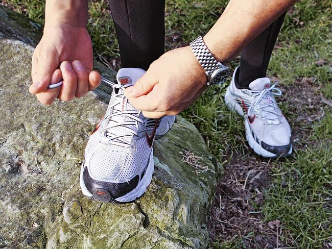 Läufer hat seinen rechten Fuss auf einen Stein aufgestellt und bindet die Schnürsenkel seines weissen Laufschuhs.