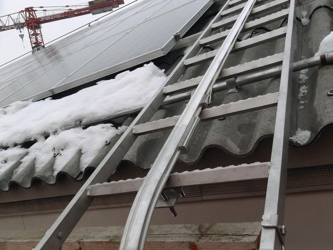 Teilaufnahme einer Dachleiter mit Fallschutzschiene, an der eine Seilsicherung befestigt werden kann.