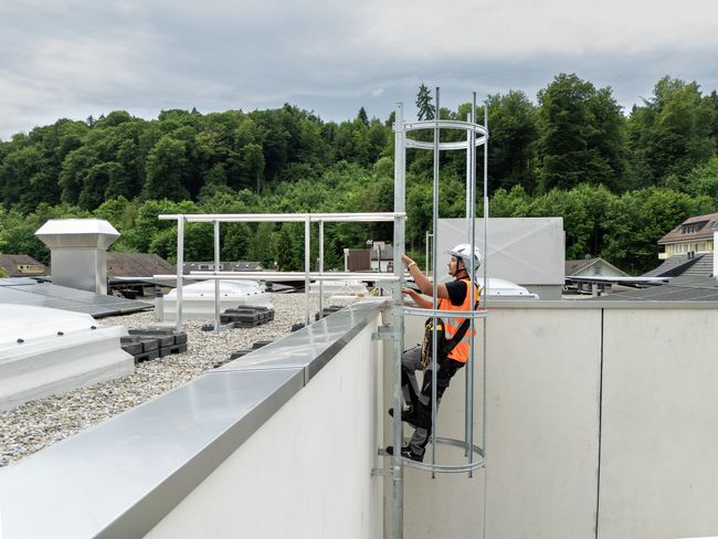 Arbeiter steigt mit Leiter sicher auf Dach.