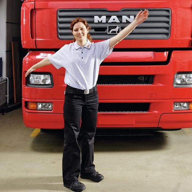 Une femme se tient devant un camion. Ses bras sont tendus à l’horizontale et elle les balance légèrement.