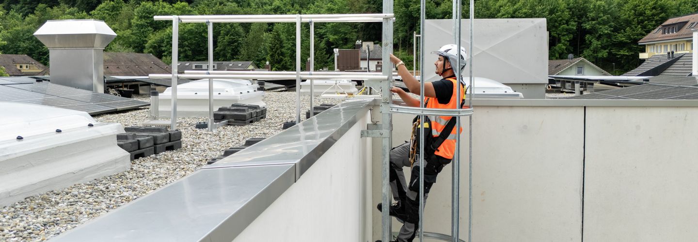 Arbeiter steigt mit Leiter sicher auf Dach.
