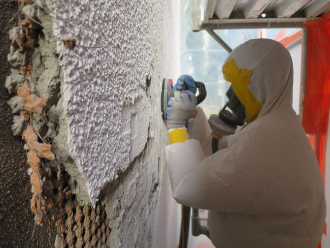 Un désamianteur en combinaison de protection avec appareil de protection respiratoire ponce du crépi amianté.