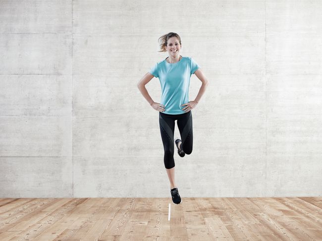 Eine Frau in Sportkleidung springt auf einem Bein über eine Linie.