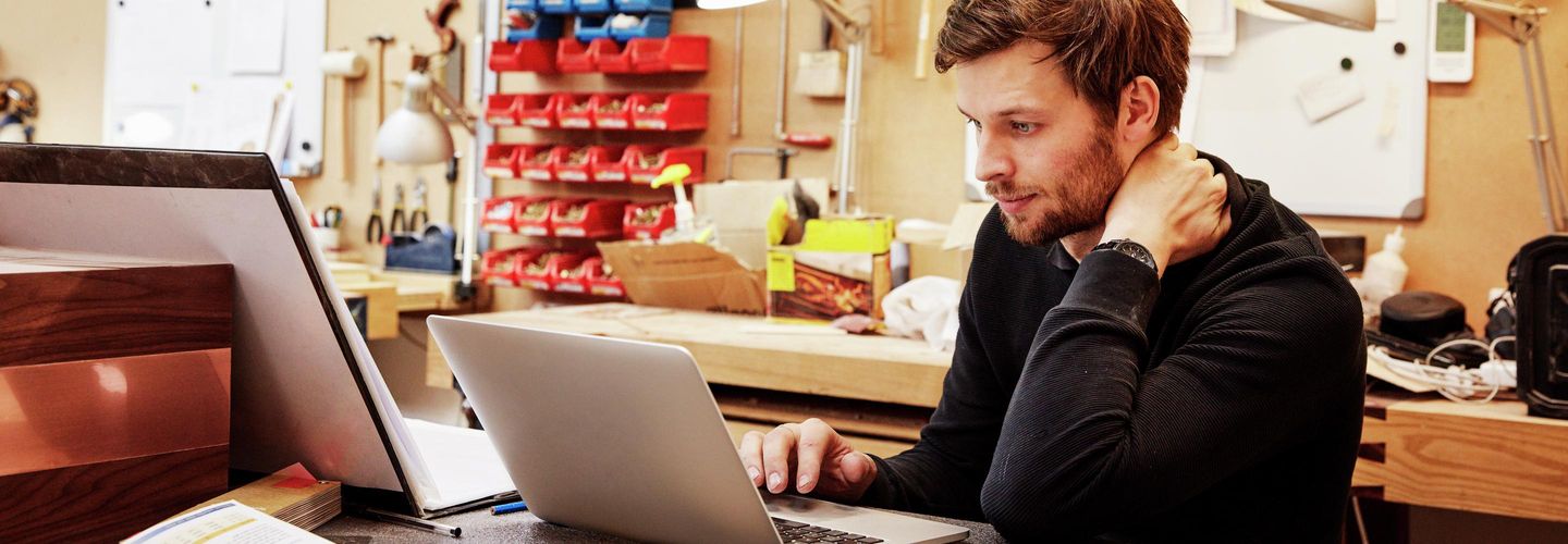 Bild eines jungen Mannes am Arbeitsplatz, arbeitend an Laptop