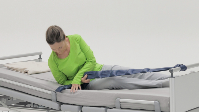 On voit une femme sur son lit médicalisé. Une bride de lit permet à la patiente de se redresser seule en position assise.