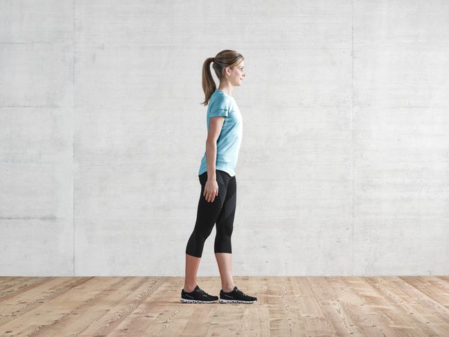 une femme en tenue de sport fait un exercice: ses pieds sont posés l’un derrière l’autre. La pointe du pied gauche touche le talon droit.