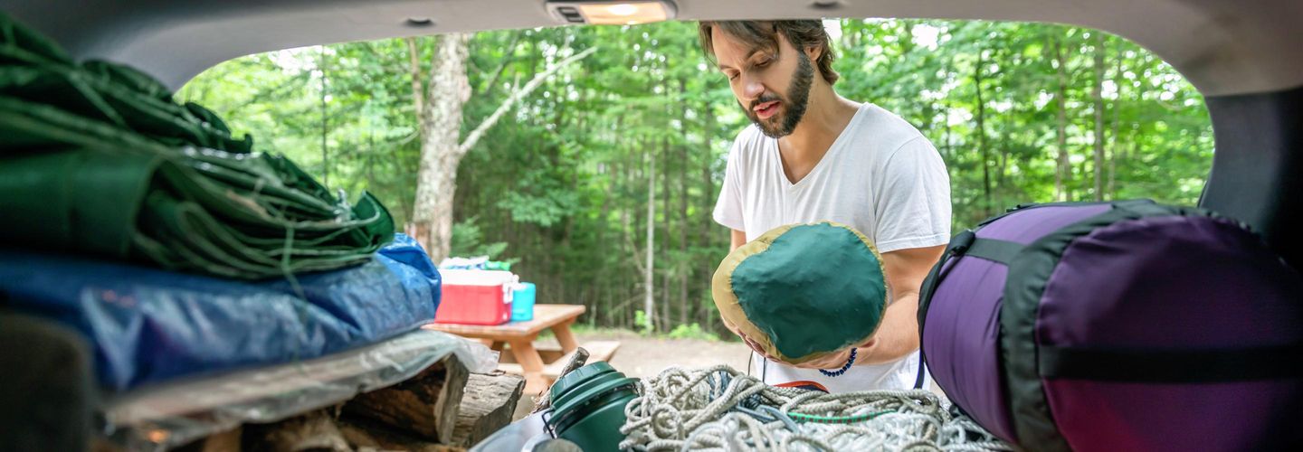 Mann entlädt das Auto mit Gepäck und anderen Gegenständen für Roadtrip und Camping