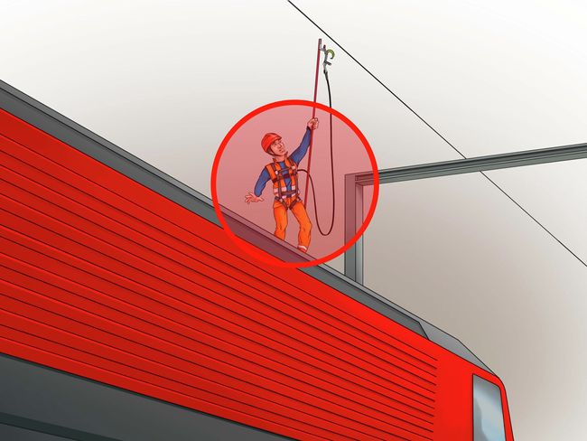 Thomas S. è in piedi sul tetto del treno e tenta di fissare la fune di trattenuta alla fune di sicurezza sopra il treno stando in piedi. È cerchiato in rosso.