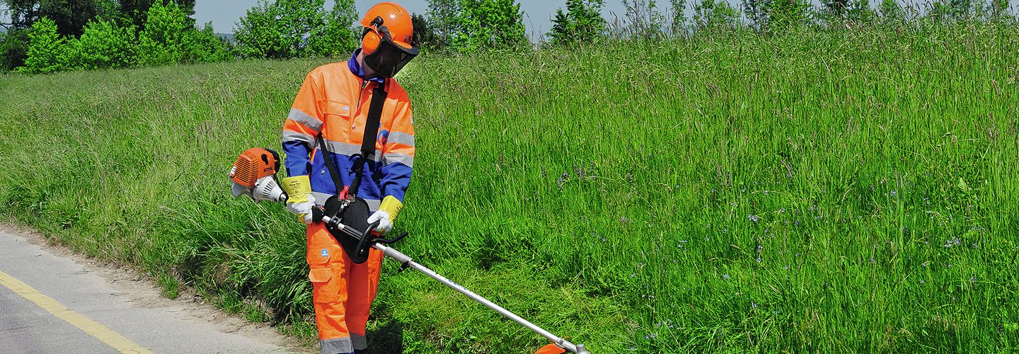 Arbeiter mit Freischneidegerät schneidet Wiese