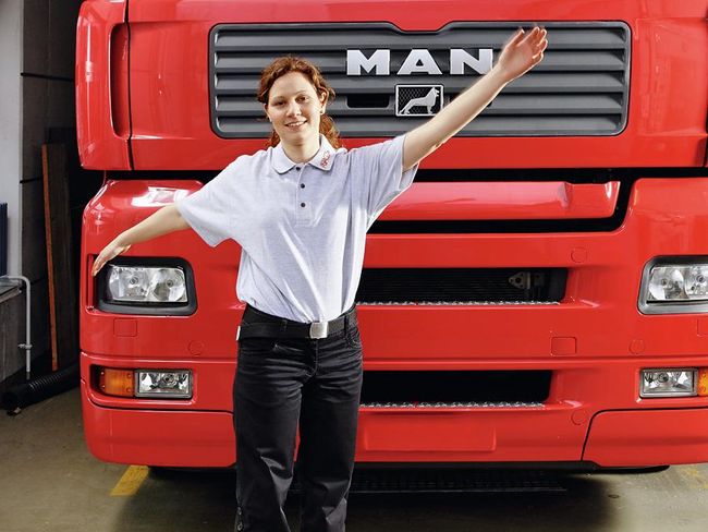 Une femme se tient devant un camion. Ses bras sont tendus à l’horizontale et elle les balance légèrement.