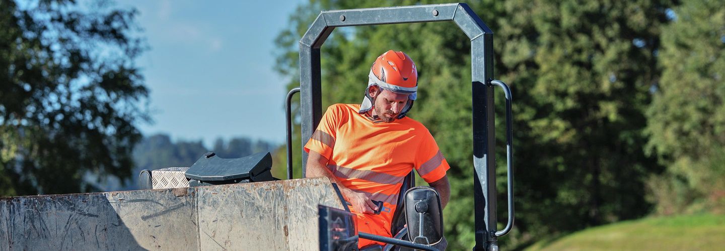 Ein Arbeiter sitz in einer Baumaschine und will sich angurten.