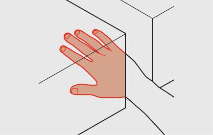 Un membro del personale tiene la mano in un'apertura tra due piani verticali. Lo spazio minimo tra questi due piani è in questo caso di 100 mm. La mano è colorata di rosso.