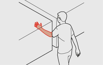 Ein Mitarbeiter hält seinen Arm in eine Öffnung zwischen zwei vertikalen Ebenen. Der Mindestabstand zwischen diesen Ebenen beträgt hier 120 mm. Der Arm ist rot eingefärbt.