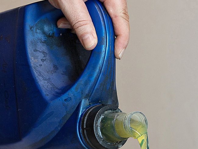 Un liquido giallastro viene versato da un contenitore blu tenuto con una mano nuda.