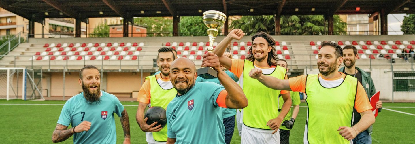 Fussballspieler laufen zusammen und halten den Pokal, den sie gerade gewonnen haben. 