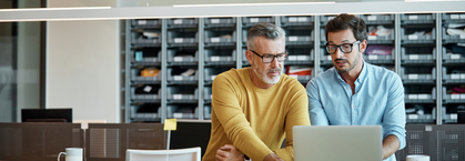 Geschäftsleute, die mit Laptop zusammen am Schreibtisch sitzen