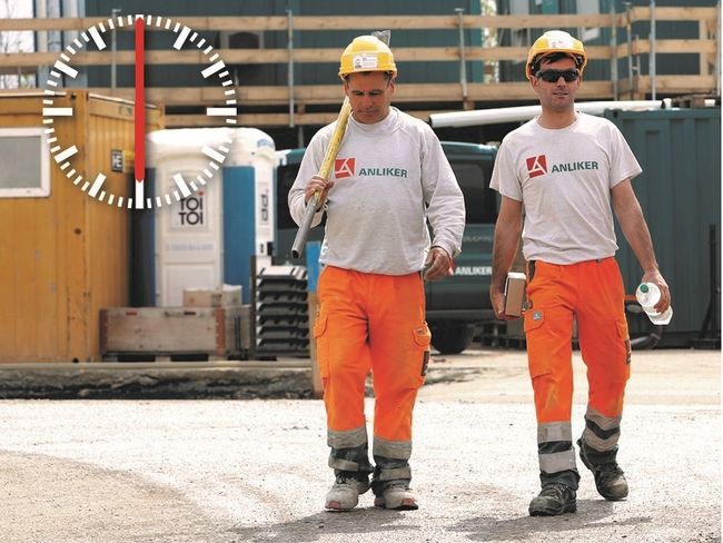 Zwei Arbeiter in oranger Arbeitshose, weissem T-Shirt und gelbem Helm auf dem Weg von der Baustelle nach Hause. Eine am linken Bildrand eingeblendete Uhr zeigt an, dass es 6 Uhr am Nachmittag ist.