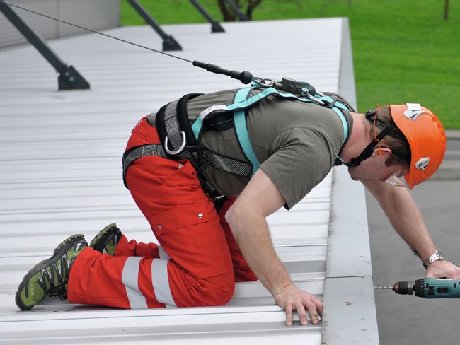 Un collaborateur se trouve sur un avant-toit, près du bord, et est équipé d’une protection par encordement. Il est assuré par une corde.