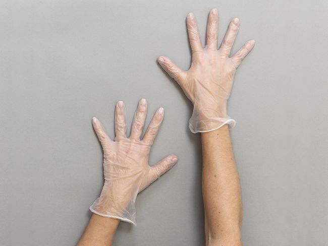 Hände mit transparenten Handschuhen aus Vinyl.