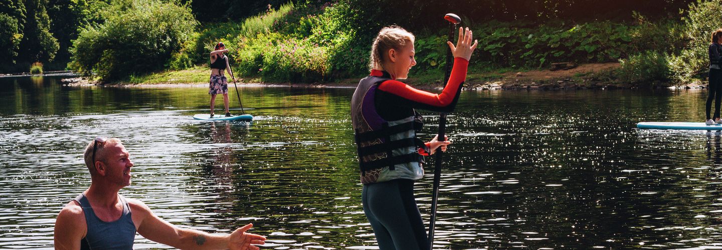 Ein Teenager-Mädchen wird von einem Wassersportlehrer im Paddleboarden unterrichtet.