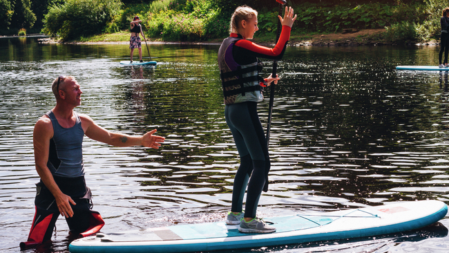 Ein Teenager-Mädchen wird von einem Wassersportlehrer im Paddleboarden unterrichtet.