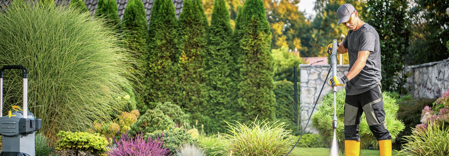 Mann, Gartenarbeit, zu Hause, Hochdruckreiniger, Käppi,  Augenschutzbrille, Schutzhandschuhe, Gummistiefel, Gartenplatten kärchern.