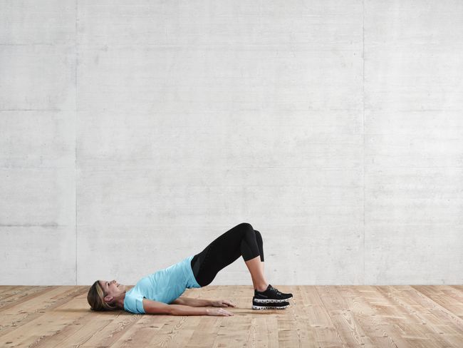 une femme en tenue de sport fait un demi-pont. Elle lève le pied droit.