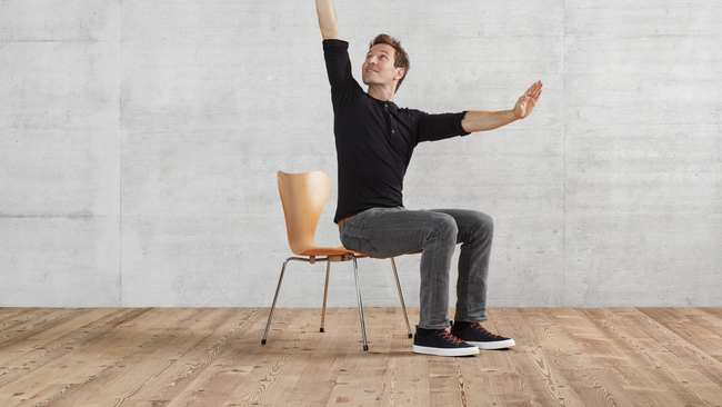 Una persona di sesso maschile in posizione seduta esegue un esercizio di mobilità con le braccia distese, tra loro ad angolo retto