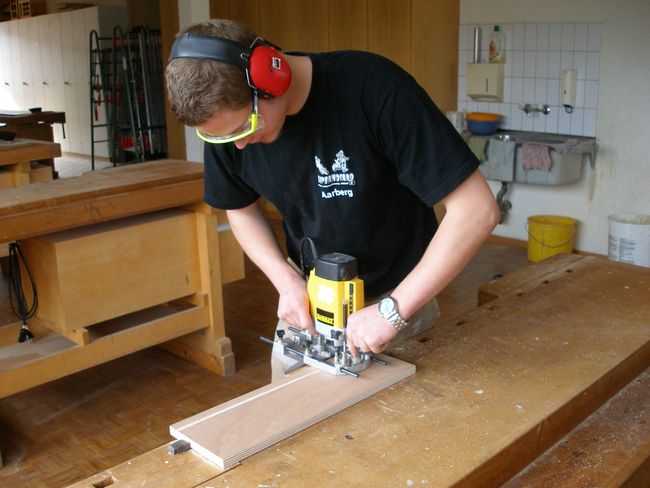 Schreiner mit Bügelschutzbrille und Gehörschutz beim Bearbeiten eines Werkstücks.