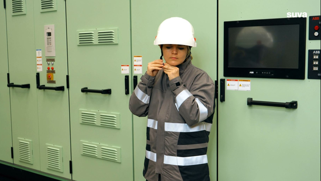Une électricienne porte une veste de protection et un casque.