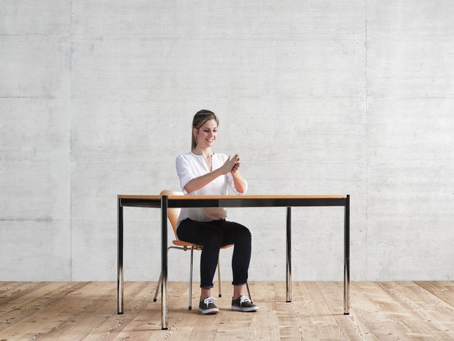 Weibliche Person sitzt am Schreibtisch und reibt ihre Handflächen aneinander