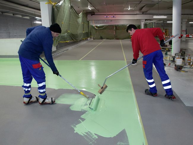 Zwei Arbeiter verteilen Epoxidharz mit Malerrolle und Schaber auf dem Boden.