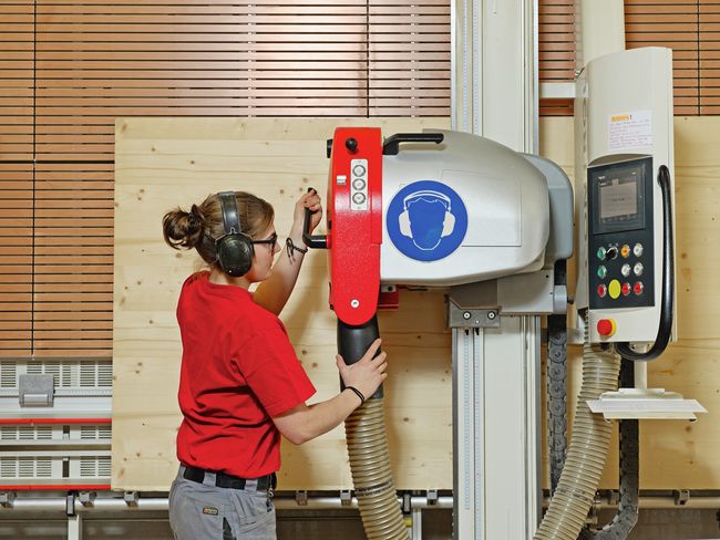 Falegname con protezione dell'udito mentre lavora a una sezionatrice verticale per pannelli.
