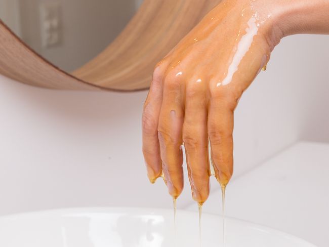 Symbolbild: Eine Hand, von der Öl in ein Waschbecken tropft.