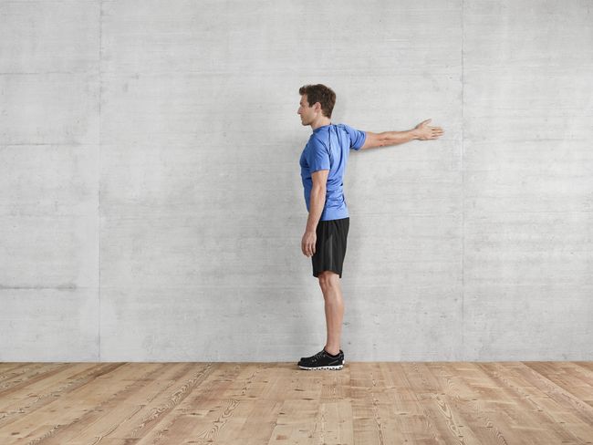 A una parete, un uomo esegue un esercizio di allungamento dei muscoli pettorali.