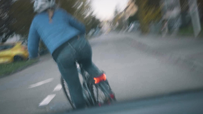 Une cycliste tourne à gauche devant une voiture sans faire de signe de la main.