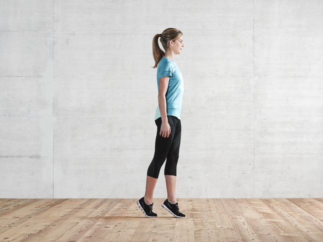 une femme en tenue de sport se tient sur la pointe des pieds. Son pied droit est derrière le pied gauche.