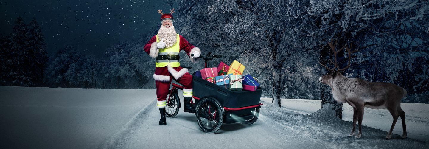 Weihnachtsmann im Schnee mit Renntier und Lastenrad mit Geschenken